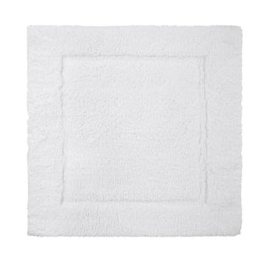 The Yves Delorme Prestige Bath Mat in Blanc is rectangular and fluffy, made from 100% cotton. It features a plush cut pile with a textured border and a non-slip backing for added safety.