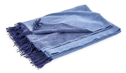 The Matouk Paley Cashmere Throw, featuring a folded oversized design in blue and light blue with fringed edges, enhances any room with comfort and style.