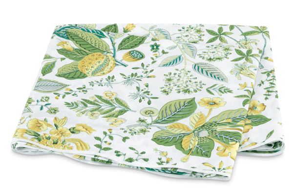 A folded fabric featuring a floral pattern with green leaves and yellow flowers on a white Matouk Pomegranate Bedding Collection, Citrus background.