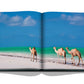 Open book featuring a photograph of two camels on a sandy beach by the Red Sea with clear blue water in the background, Red Sea: The Saudi Coast by Assouline.