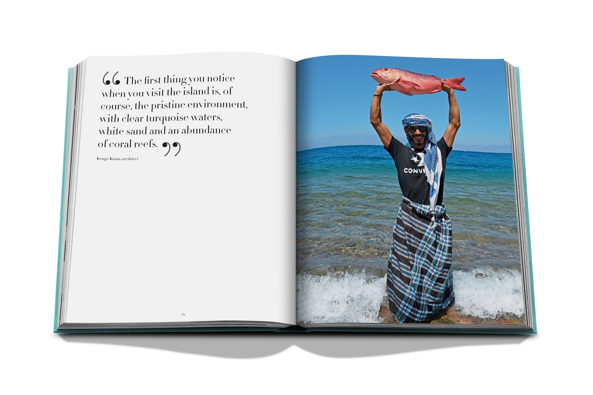 Open book showing a photo of a smiling man in sunglasses and a cap, standing in shallow water of the Red Sea and holding a large fish, with text describing a tropical location from "Red Sea: The Saudi Coast" by Assouline.