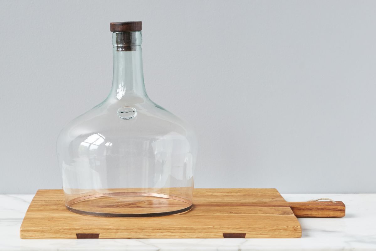 The Rectangle Oak Medium Charcuterie Board by etúHOME features a large clear glass cloche with a wooden knob, elegantly displayed against a light gray background.