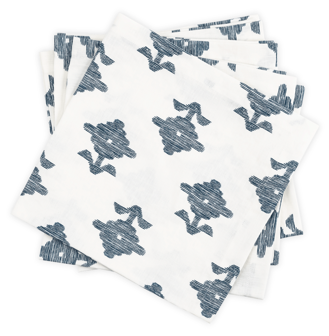 A stack of Matouk's Rubia Navy Napkin Set, featuring white OEKO-TEX® Standard 100 certified napkins with a blue floral pattern, is arranged slightly askew on a black background.