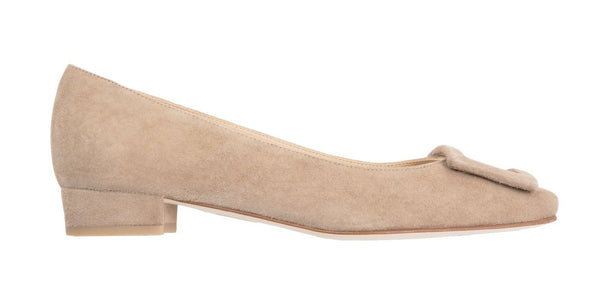 A beige calf suede low-heel pump with a decorative bow on the toe, isolated on a white background, the Ann Mashburn Suede Buckle Shoe.