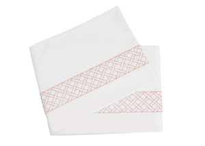 Two elegantly folded sheets in white, featuring a salmon geometric pattern along the edges, crafted from luxurious Egyptian cotton percale. This exquisite set is part of the HIVE Exclusive Matouk Rovella Bedding Collection and is proudly OEKO-TEX® certified for quality and sustainability.