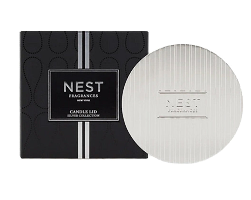 The Nest Silver Classic Candle Lid is shown next to its black box with a vertical silver stripe, highlighting its design for fragrance preservation.