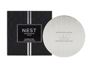 The Nest Silver Classic Candle Lid is shown next to its black box with a vertical silver stripe, highlighting its design for fragrance preservation.