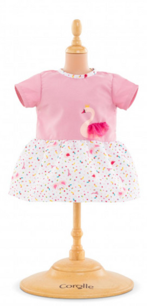 A pink short-sleeved Corolle Baby Doll Swan Royal Dress with a flamingo print on the chest and a white, multicolored confetti-patterned skirt, displayed on a wooden mannequin.