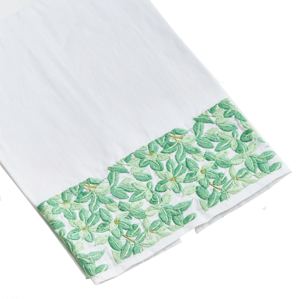 A Haute Home Boxwood Tip Towel, a white linen cloth with a decorative green floral pattern along one edge, isolated on a black background.