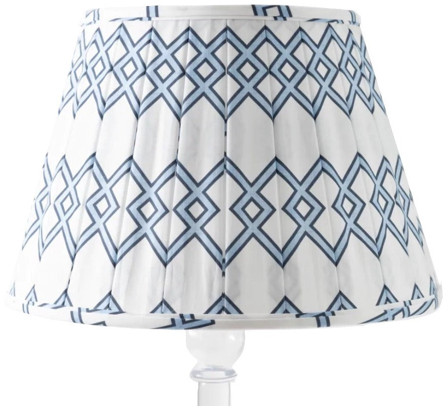 The Lattice Shade in Blue by Sorella Glenn features a geometric blue diamond pattern and box pleat detail, shown on a clear base—perfect for adding a classic preppy touch to any room.