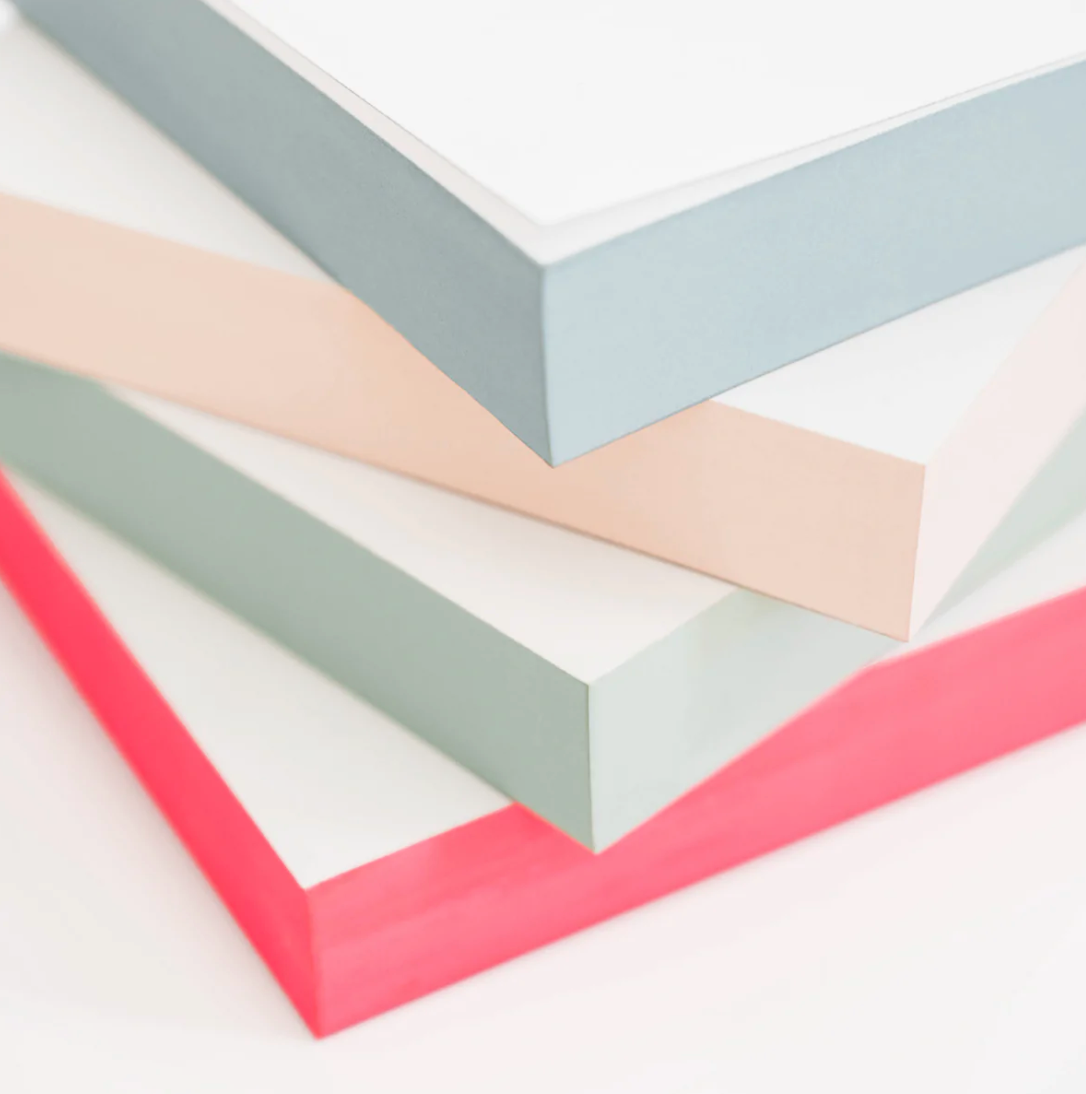 Four stacks of Sugar Paper's Green Painted Pad, each with thick gray, beige, light green, and pink edges, are layered atop one another against a white background—perfect for everyday on-the-go notes.