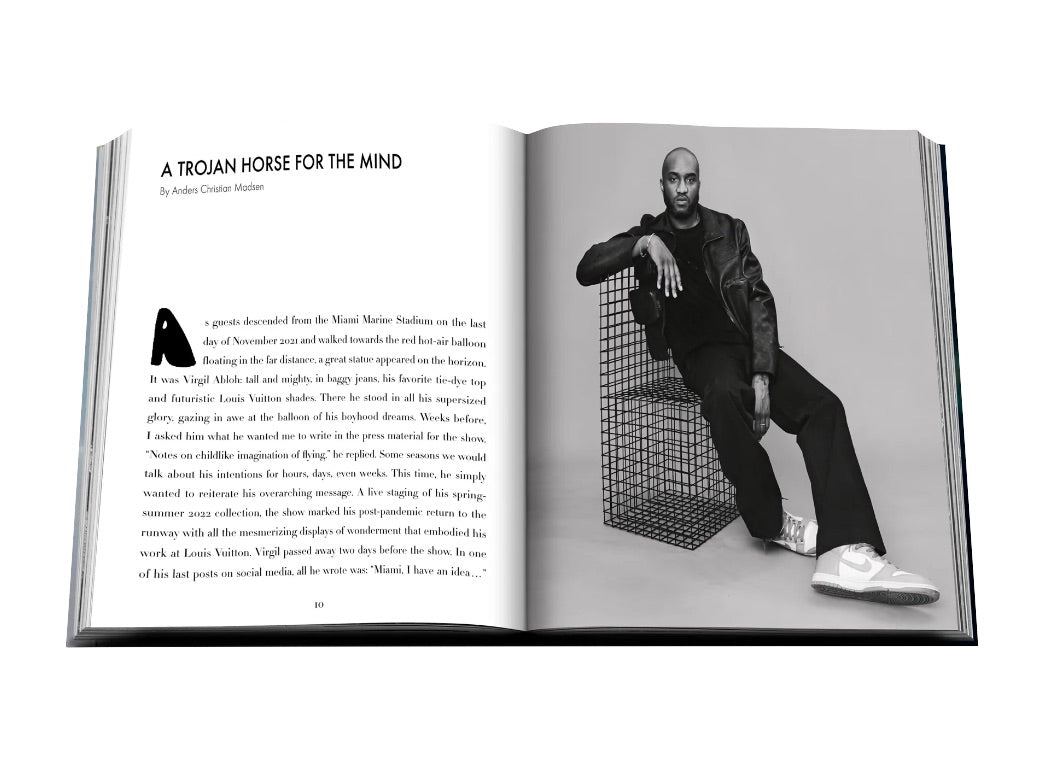 An open magazine displays an article titled "A Trojan Horse for the Mind" with an image of a person sitting on a black wire structure. The individual, clad in a dark outfit and white sneakers, evokes the essence of Assouline's vision for Louis Vuitton: Virgil Abloh.