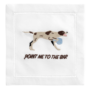 Add humor to your table with August Morgan’s "Point Me To The Bar" Cocktail Napkins, featuring a linen design with an embroidered brown and white dog holding a blue ball above playful text.