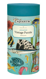 The Aquarium 1,000 Piece Puzzle by Cavallini Papers and Co comes in a cylindrical box featuring vibrant fish and plant illustrations—a challenging puzzle ideal for enthusiasts.