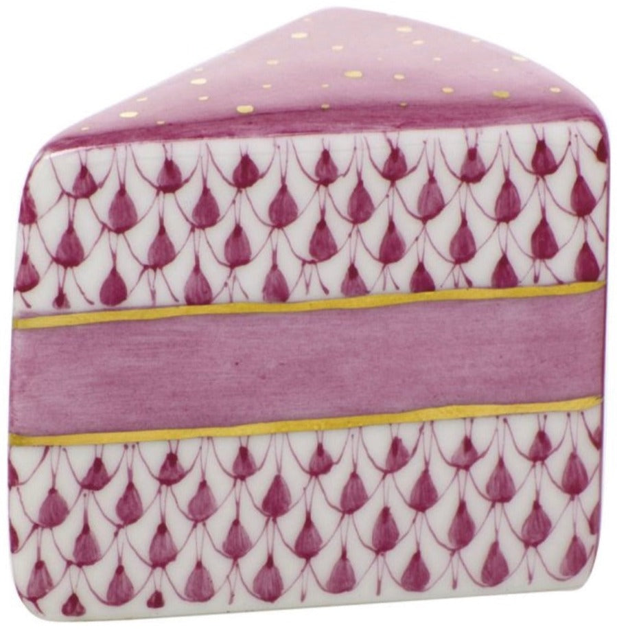 The Herend Slice of Cake is a ceramic piece shaped and painted to look like a cake slice, featuring hand-painted purple and gold decorative designs that showcase artistic craftsmanship.