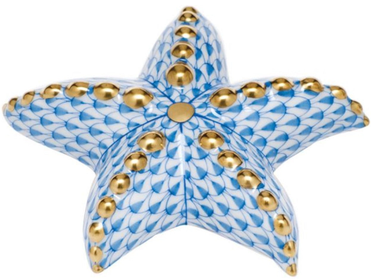 The Herend Puffy Starfish is a ceramic piece inspired by hand-painted designs, showcasing a blue scale-like pattern and gold accents on each arm, displayed from above on a white background.