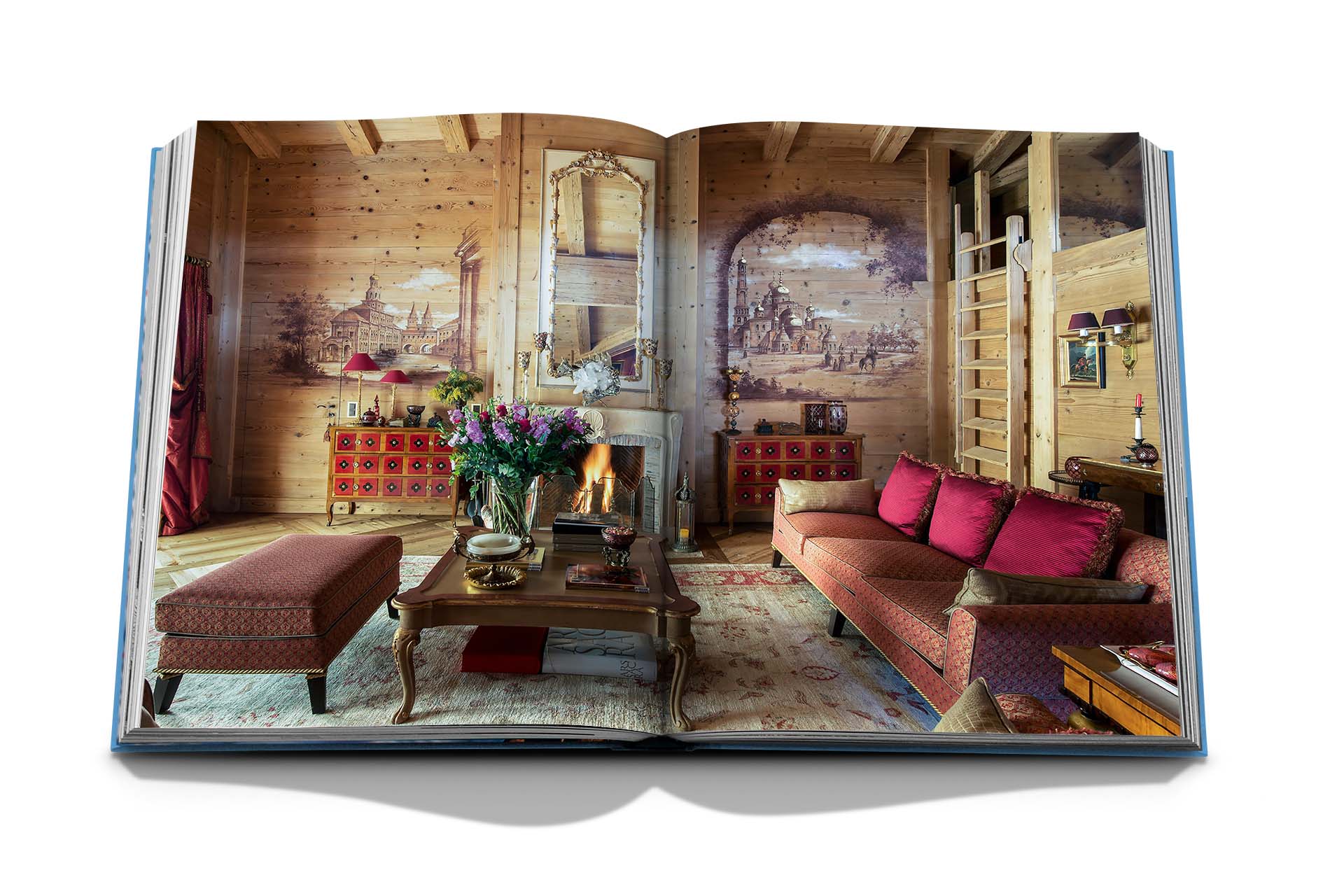 An open book displaying a photo of a cozy living room with wooden walls, red furniture, a fireplace, and an ornate mirror. The room exudes Alpine chic with its classic, rustic design and detailed wall art, reminiscent of the charming chalets in Gstaad in the Swiss Alps. The book is titled "Gstaad Glam" and is published by Assouline.