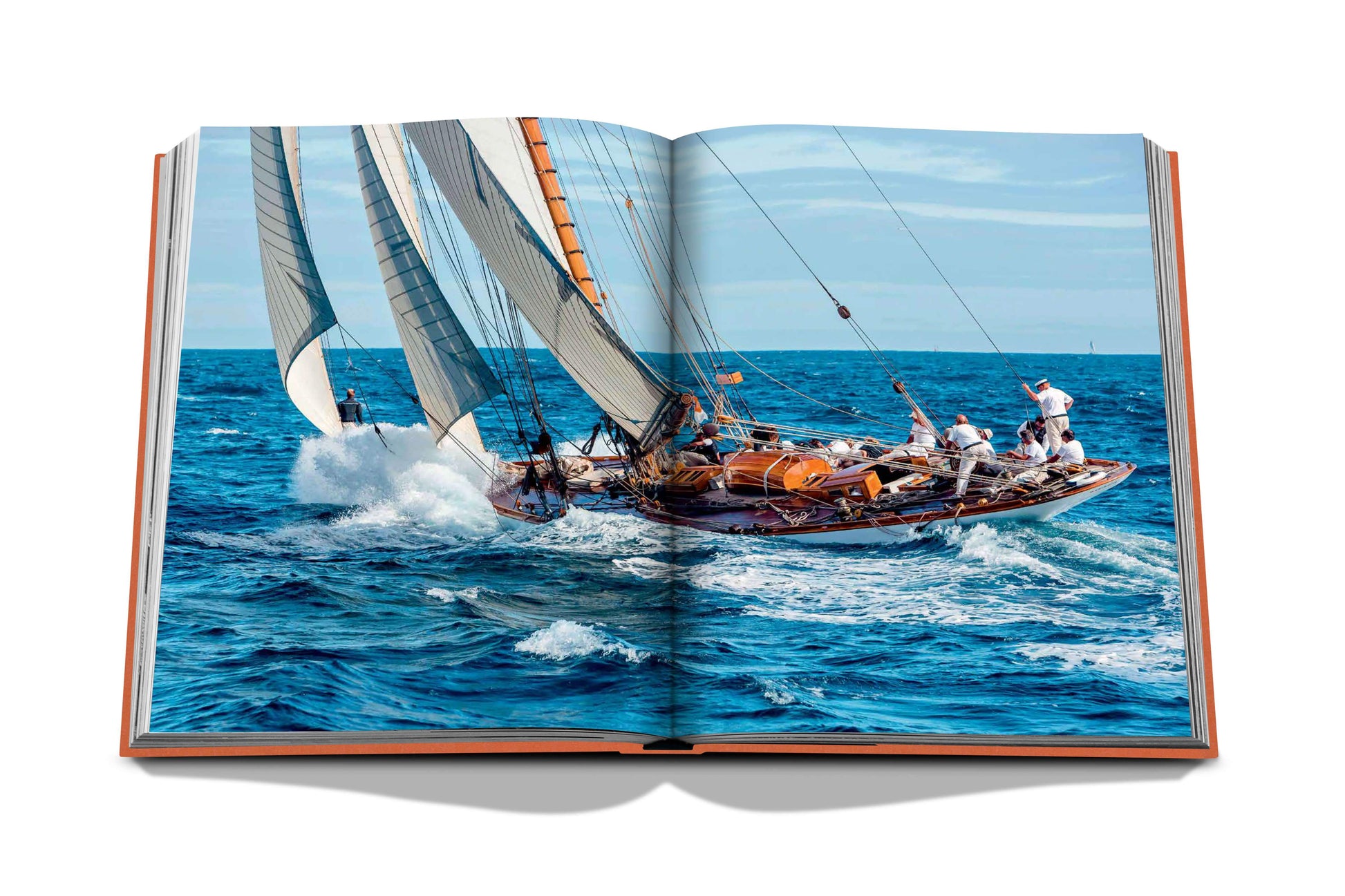 Open book with a photograph of a sailboat navigating through rough ocean waves, crew members managing the sails, capturing the thrill of St Tropez Soleil by Assouline.