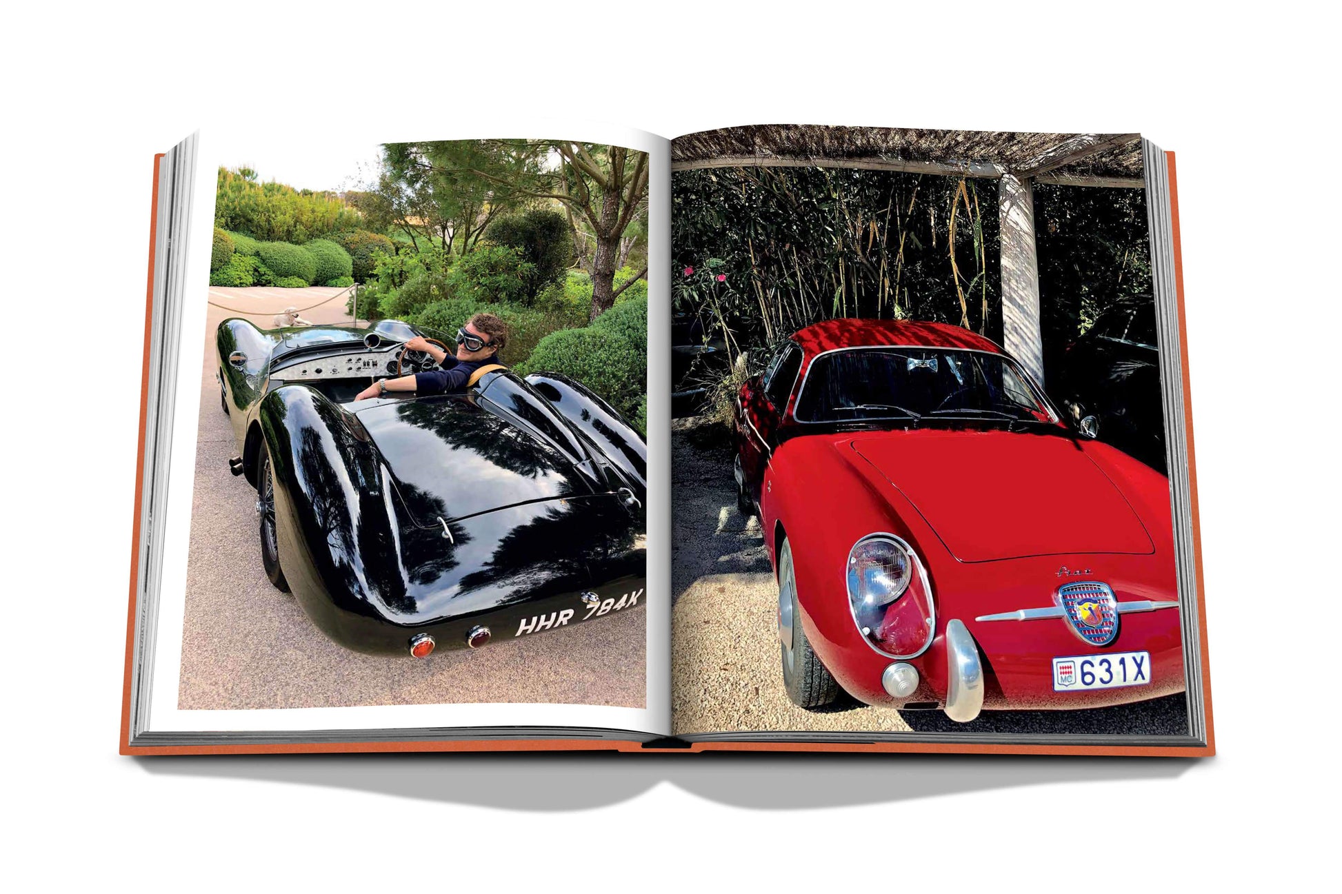 An open book displays two classic cars: a black roadster with a driver on the left page and a red vintage coupe parked under a wooden structure on the right page, reminiscent of scenes from St Tropez Soleil by Assouline.