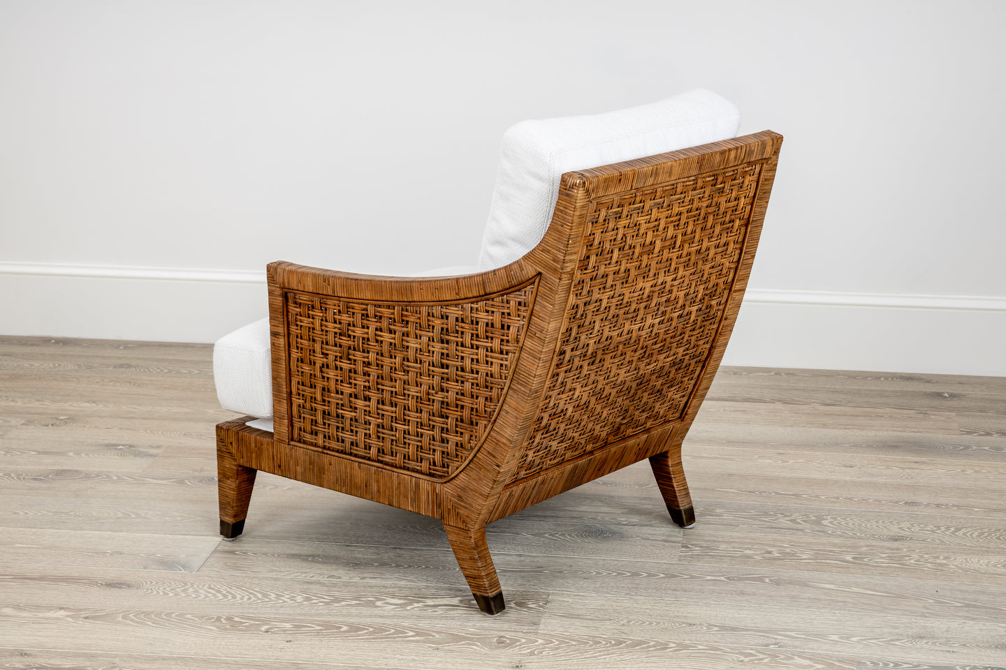 A St. Germaine Chair by McGuire Furniture, featuring a white cushion and elegant cane wrap design, rests on a light wood floor against a pristine wall.