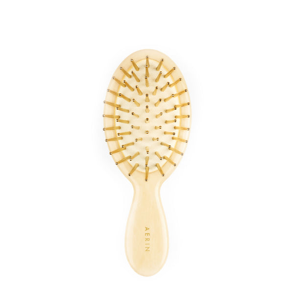 A small AERIN Travel Ivory Hairbrush with gold bristles, handcrafted in Italy.