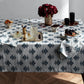A sunlit dining table with a wooden floor is set with drinks, snacks, fruit, candles, red flowers in a vase, and Matouk Rubia Navy Placemats (set of 4).