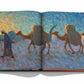 A page from "Uzbekistan: Avant-Garde Orientalists" by Assouline displays an impressionist painting of a person guiding three camels, rendered with vibrant, colorful brushstrokes that echo the style of Russian avant-garde art.