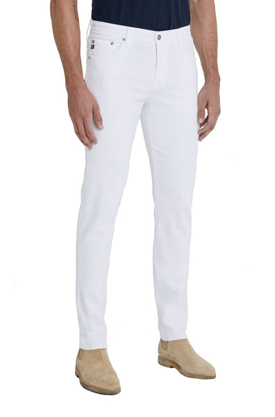 A man standing against a white background is wearing AG Jeans Tellis Modern Slim in Italian sateen fabric and beige suede shoes.