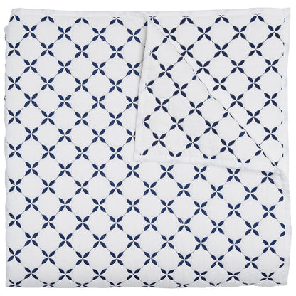 The Layla Indigo Coverlet by John Robshaw is a folded white cotton voile coverlet, hand quilted with a navy geometric pattern inspired by Mughal gardens, featuring circular four-petal motifs.
