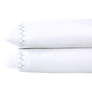 Two Stitched Light Indigo Pillowcases by John Robshaw, crafted from soft cotton percale with a blue zigzag embroidered edge, are stacked on a white background.