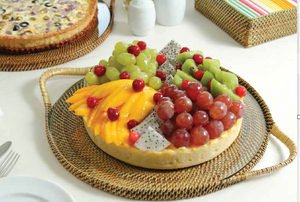 A tart with grapes, kiwi, dragon fruit, mango, and red berries sits on a Calaisio Round Serving Tray with Glass; other desserts and napkins appear in the background.