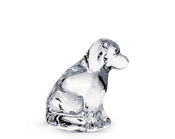 The Simon Pearce Glass Puppy is a clear glass figurine of a sitting dog, viewed from the side on a white background—an elegant nod to cherished canine companionship.