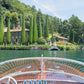 Experience La Dolce Vita with Gray Malin’s “Afternoon Ride Lake Como,” a 24" x 36" framed print capturing a wooden boat gliding toward a villa amid lush gardens and hills, available in a white frame from Gray Malin.