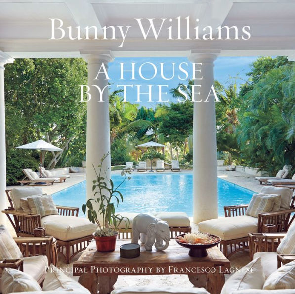 A lush outdoor seating area by a pool exudes Caribbean retreat vibes under a bright sky. The cover of "House by the Sea" by Abrams highlights its exquisite interior design.