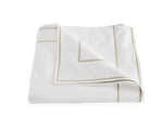 The Matouk Ansonia Bedding Collection in Almond features a neatly folded white blanket with light beige border trim, crafted from Egyptian cotton percale—a perfect touch of luxury bedding.