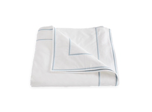 White duvet cover with light blue piping, partially folded, displayed on a plain white background, crafted from Matouk 500 thread count Egyptian cotton percale.