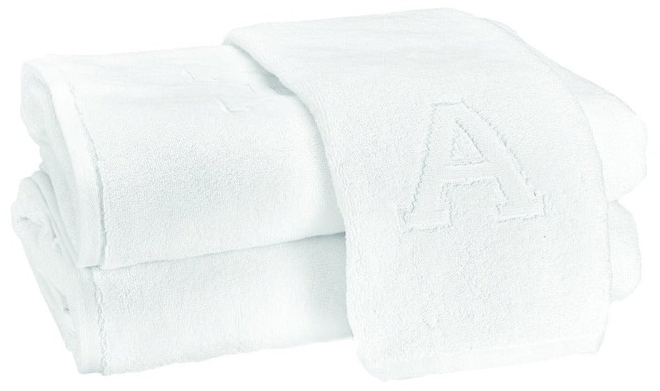 Two Auberge Monogram Bath Towels by Matouk—folded white cotton terry, one with an embroidered "A"—are stacked on a white background, adding elegant charm to any guest bath.