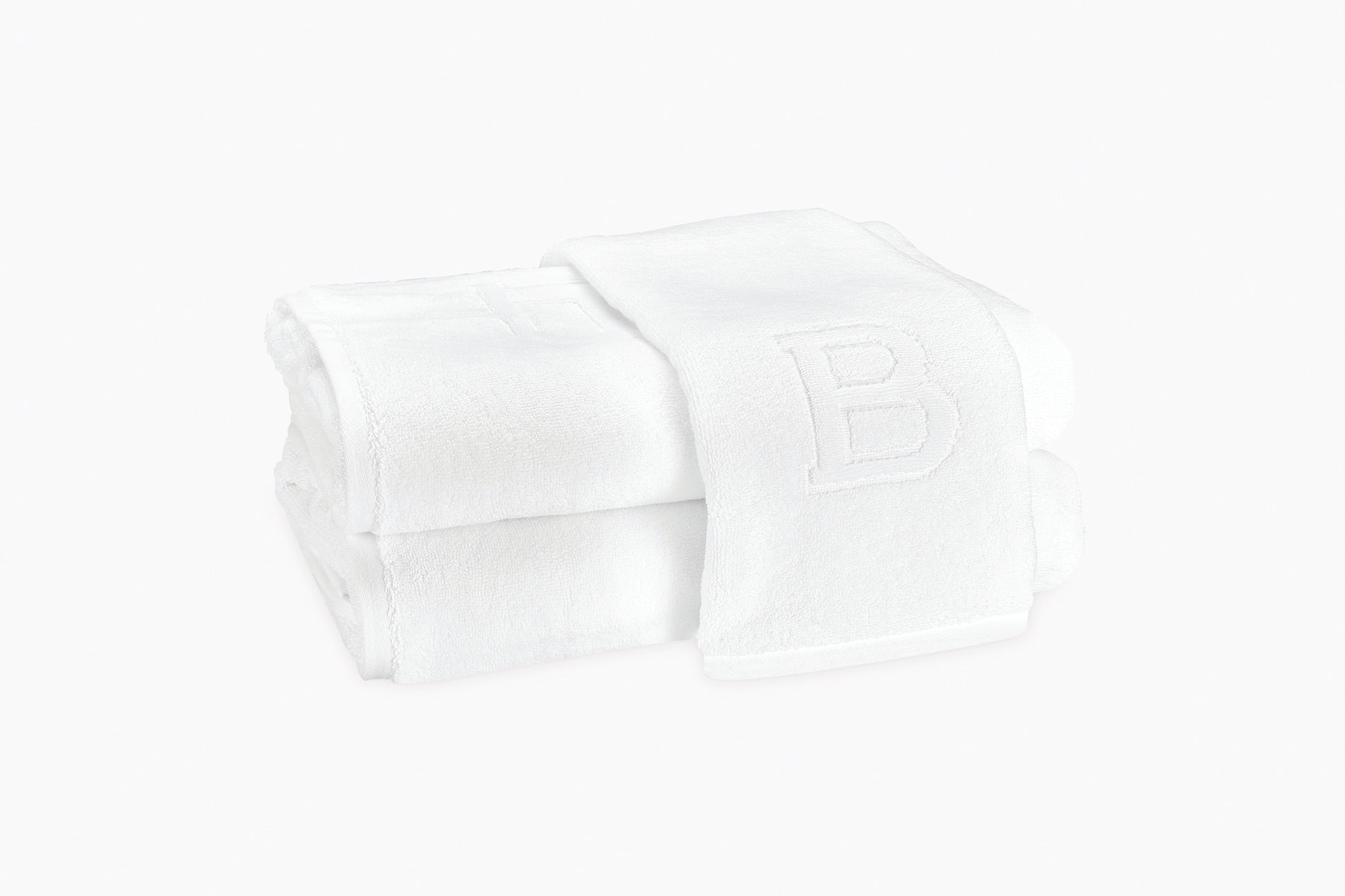 Two folded white Matouk Auberge Monogram Bath Towels, one draped over the other with an embossed "B" on top—an elegant way to bring signature Auberge luxury to your guest bath.