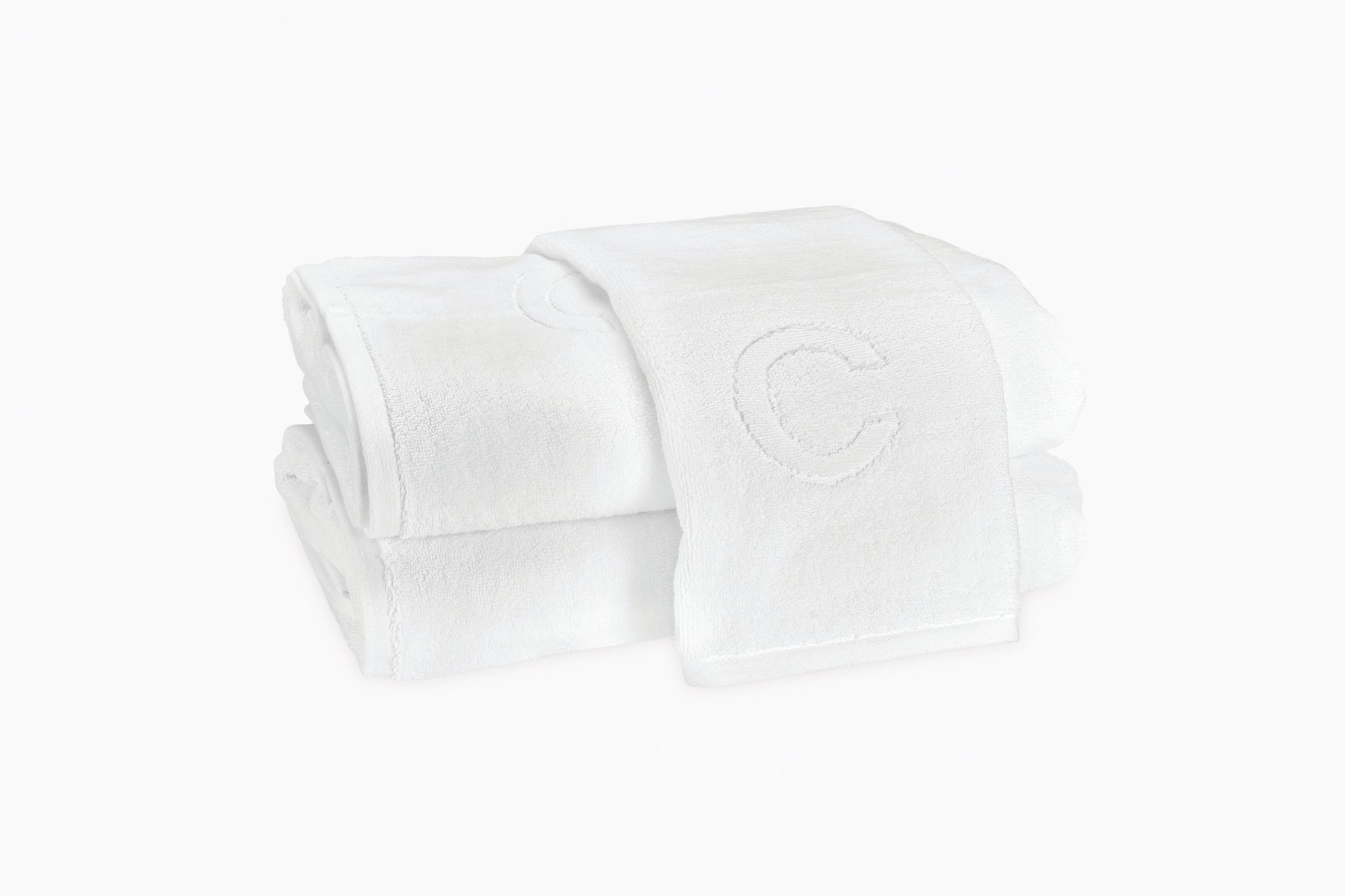 Two folded Matouk Auberge Monogram Bath Towels, styled for a guest bath and displayed on a plain white background, with the top towel featuring an embroidered letter "C" at its visible end.