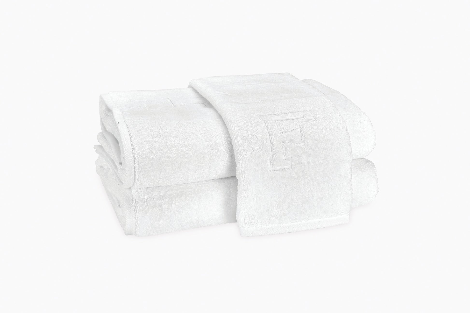 Two folded white Matouk Auberge Monogram Bath Towels, one showing an embossed "F", showcase timeless style—ideal for the guest bath. Displayed on a plain white background.