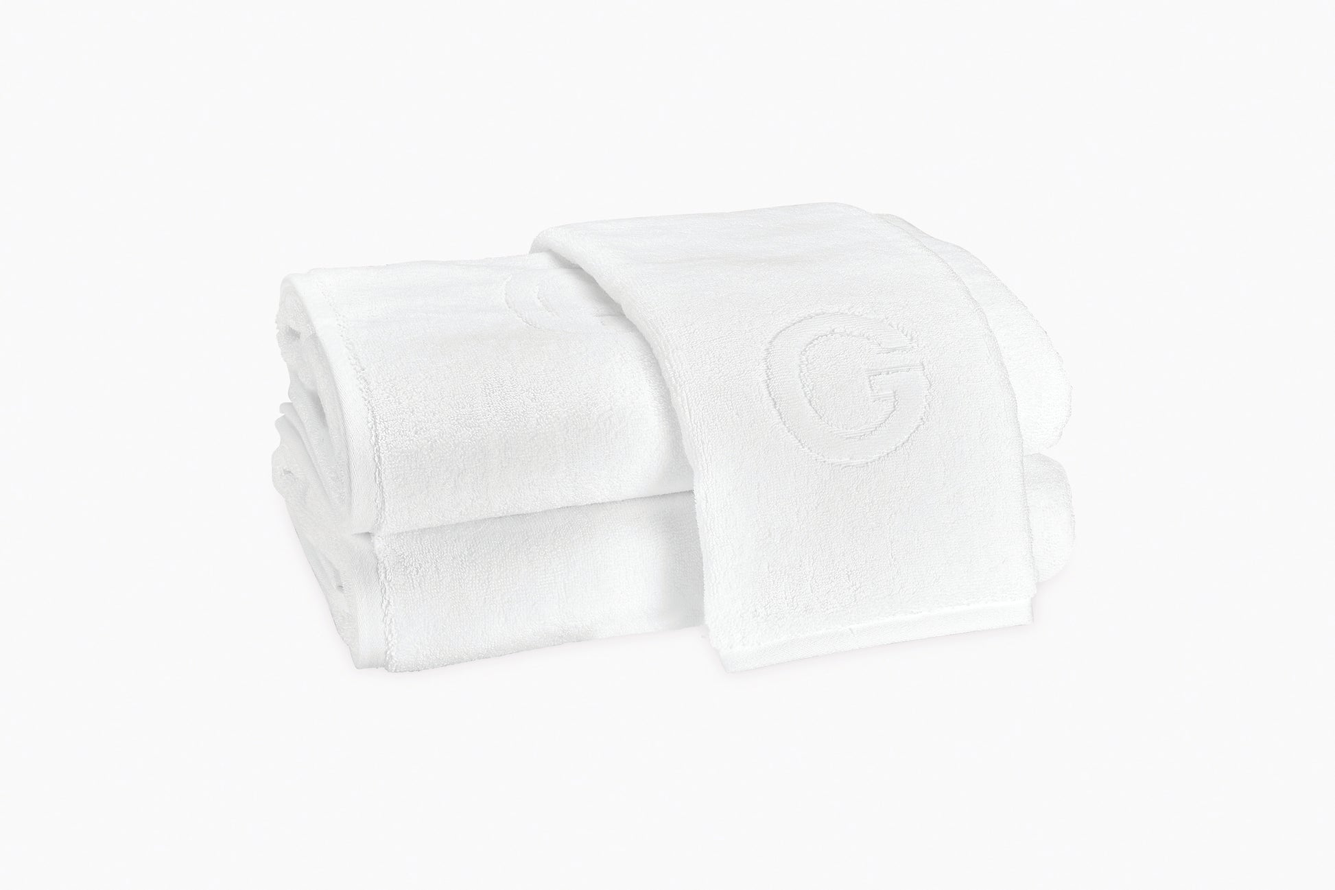 Two neatly folded Matouk Auberge Monogram Bath Towels, one draped over the other, featuring a prominent "G" embroidery—an elegant upgrade for any guest bath.