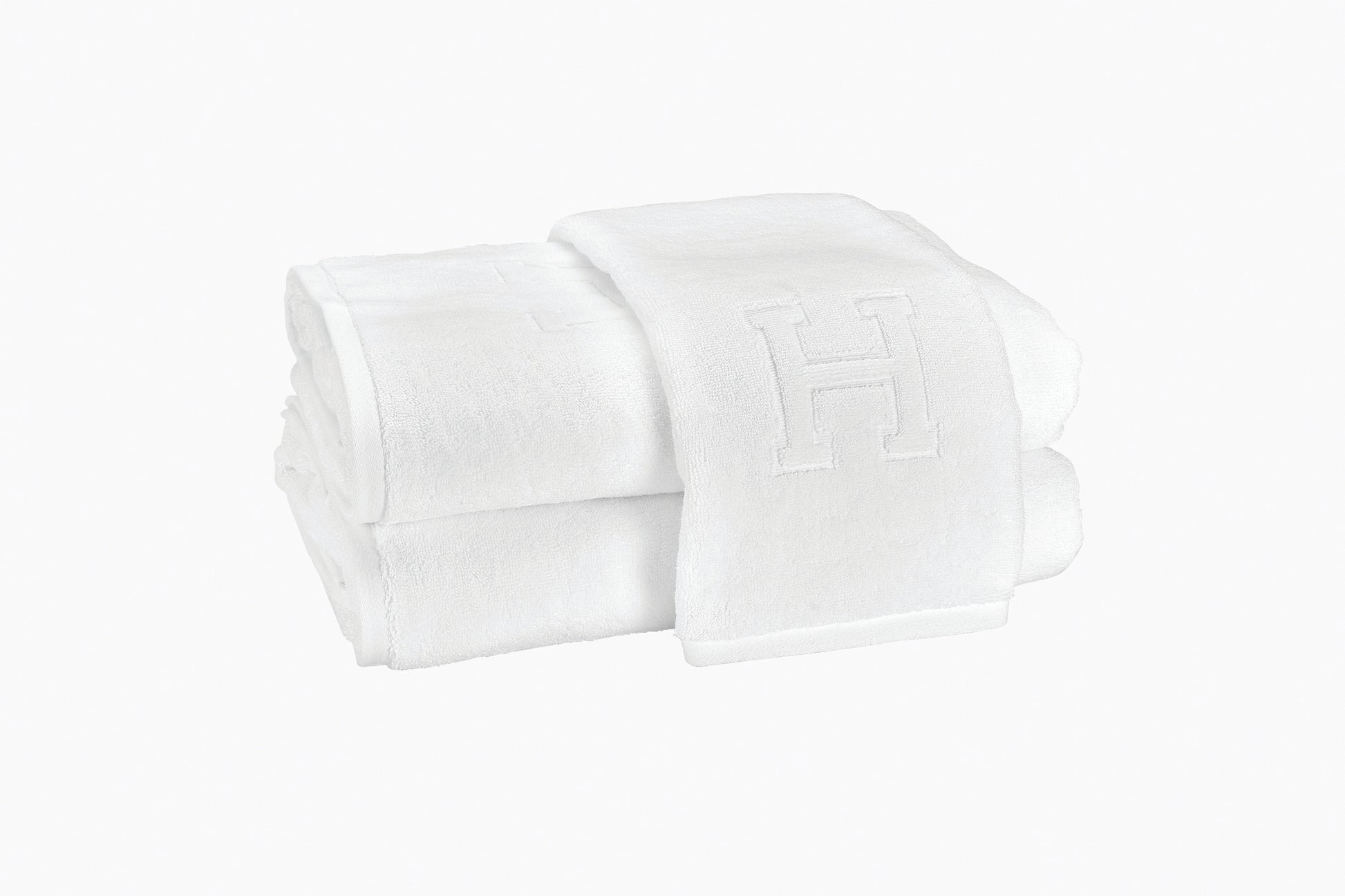 The Matouk Auberge Monogram Bath Towel is a folded white cotton terry towel featuring an embroidered "H," ideal for guest baths and shown against a plain white background.