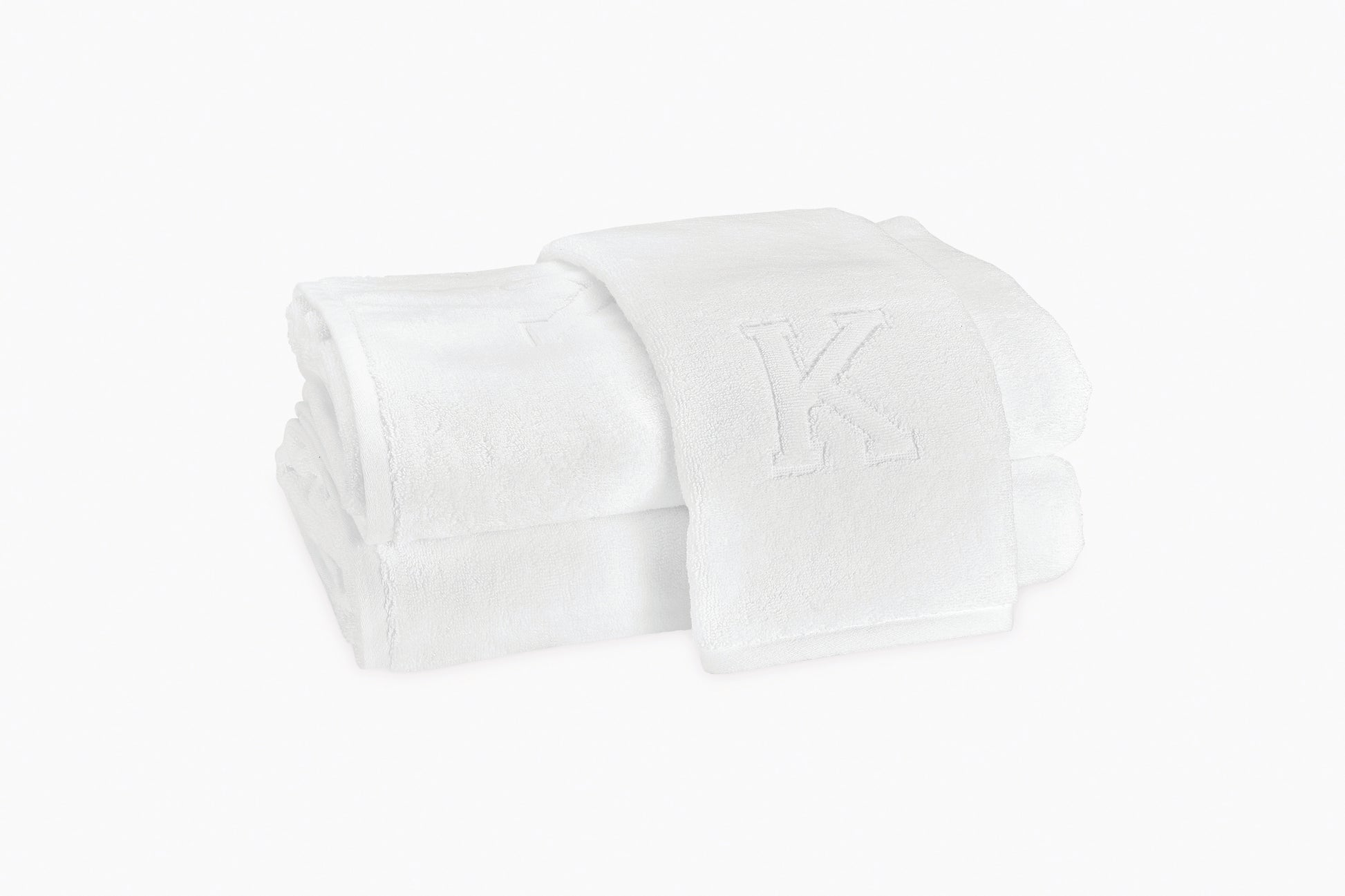 The Auberge Monogram Bath Towels by Matouk feature two white cotton terry towels, one embroidered with a "K" monogram, beautifully displayed against a plain white background—ideal for elevating any guest bath.