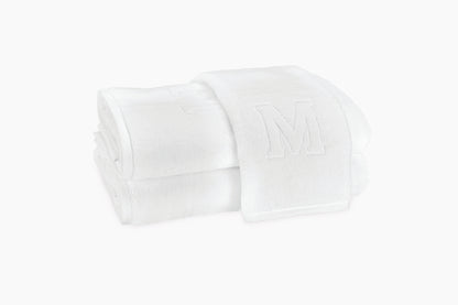 A crisp stack of Matouk Auberge Monogram Bath Towels, with an embossed "M" on top, brings refined elegance to your guest bath.