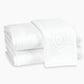 Two neatly folded white Matouk Auberge Monogram Bath Towels are stacked, one displaying an oval monogram design—ideal for elevating any guest bath.