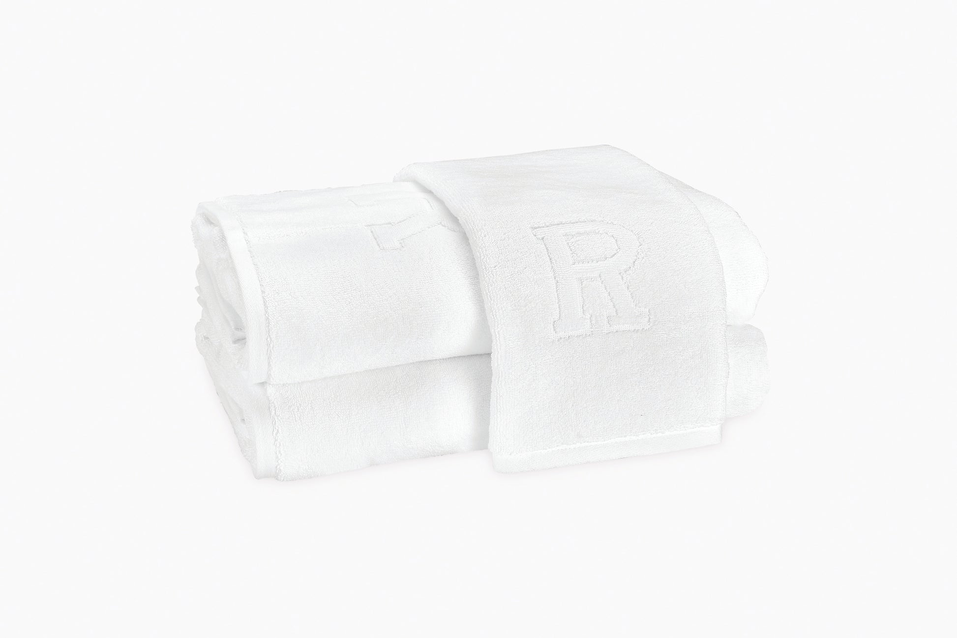 Two folded white Matouk Auberge Monogram Bath Towels are stacked, one draped over the other. Each guest towel features an embroidered letter "R," lending elegant, Auberge-inspired style.