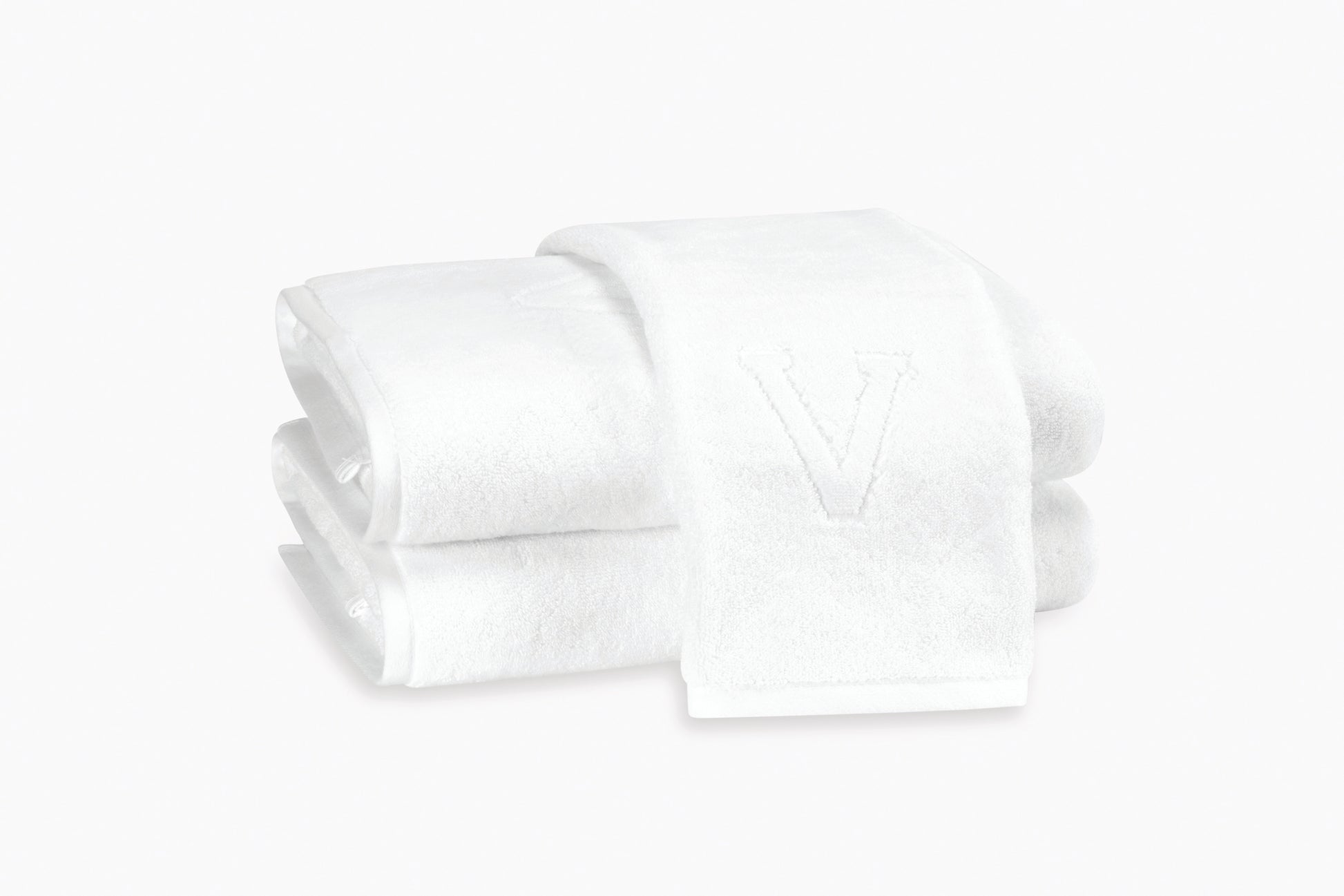 Two neatly folded white Auberge Monogram Bath Towels by Matouk, one embossed with a "V," evoke a luxury guest bath experience against a plain white background.