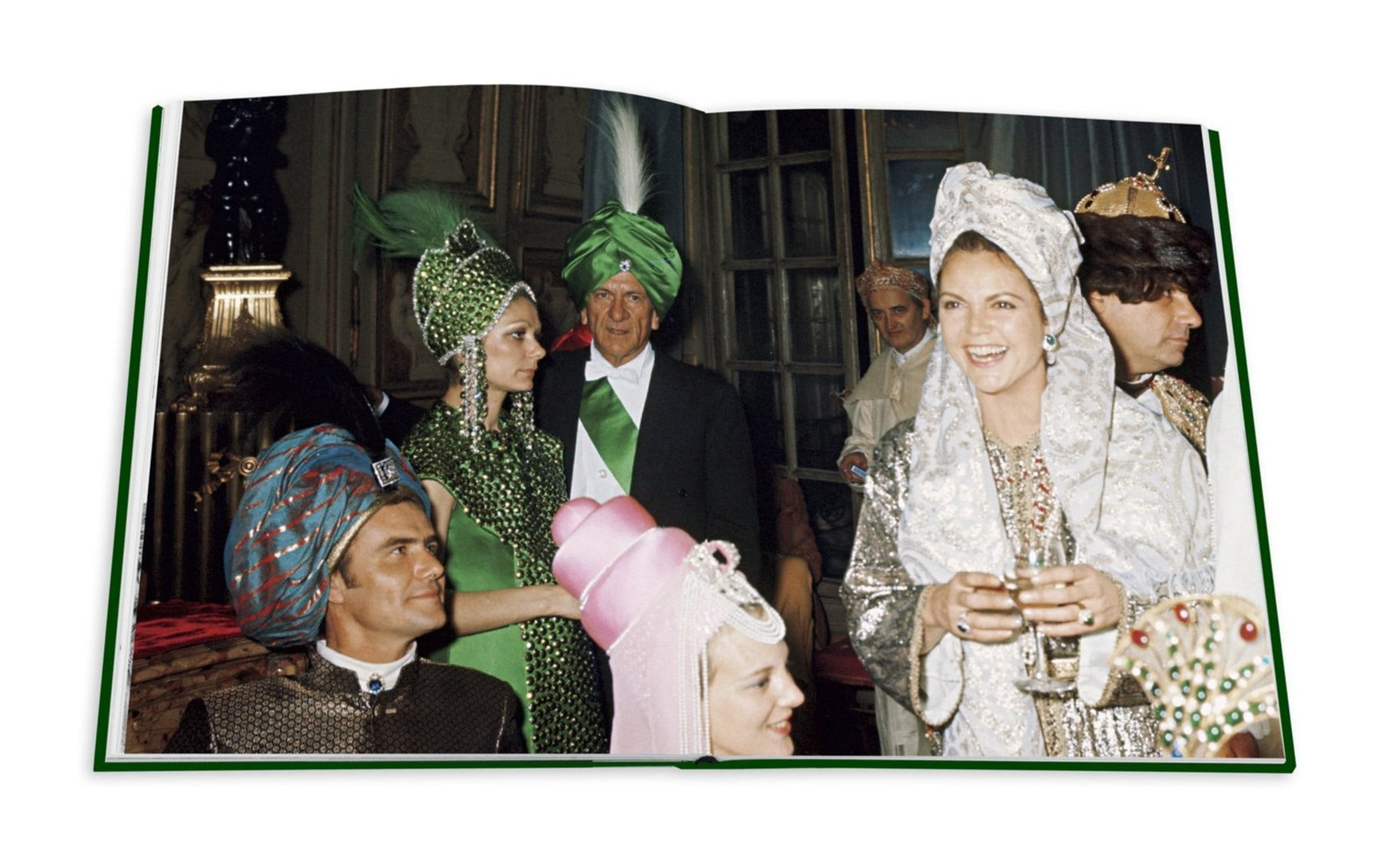 Attendees in vibrant, ornate costumes at a social gathering, channeling the Romanov dynasty's grandeur with turbans and headpieces, hold drinks and smile in a room reflecting Art Deco Paris, as featured in Assouline's "Legendary Costume Balls of the Twentieth Century.
