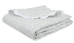 The Celine Bedding Collection in Grass by Matouk features a folded white Egyptian cotton percale blanket with green dots and an embroidered scalloped edge, neatly stacked on a white surface.