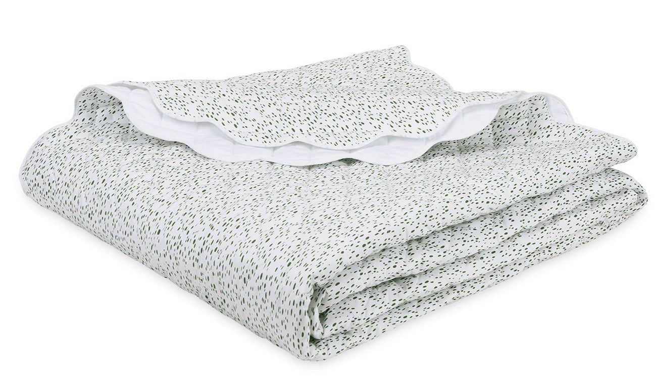 The Celine Bedding Collection in Grass by Matouk features a folded white Egyptian cotton percale blanket with green dots and an embroidered scalloped edge, neatly stacked on a white surface.